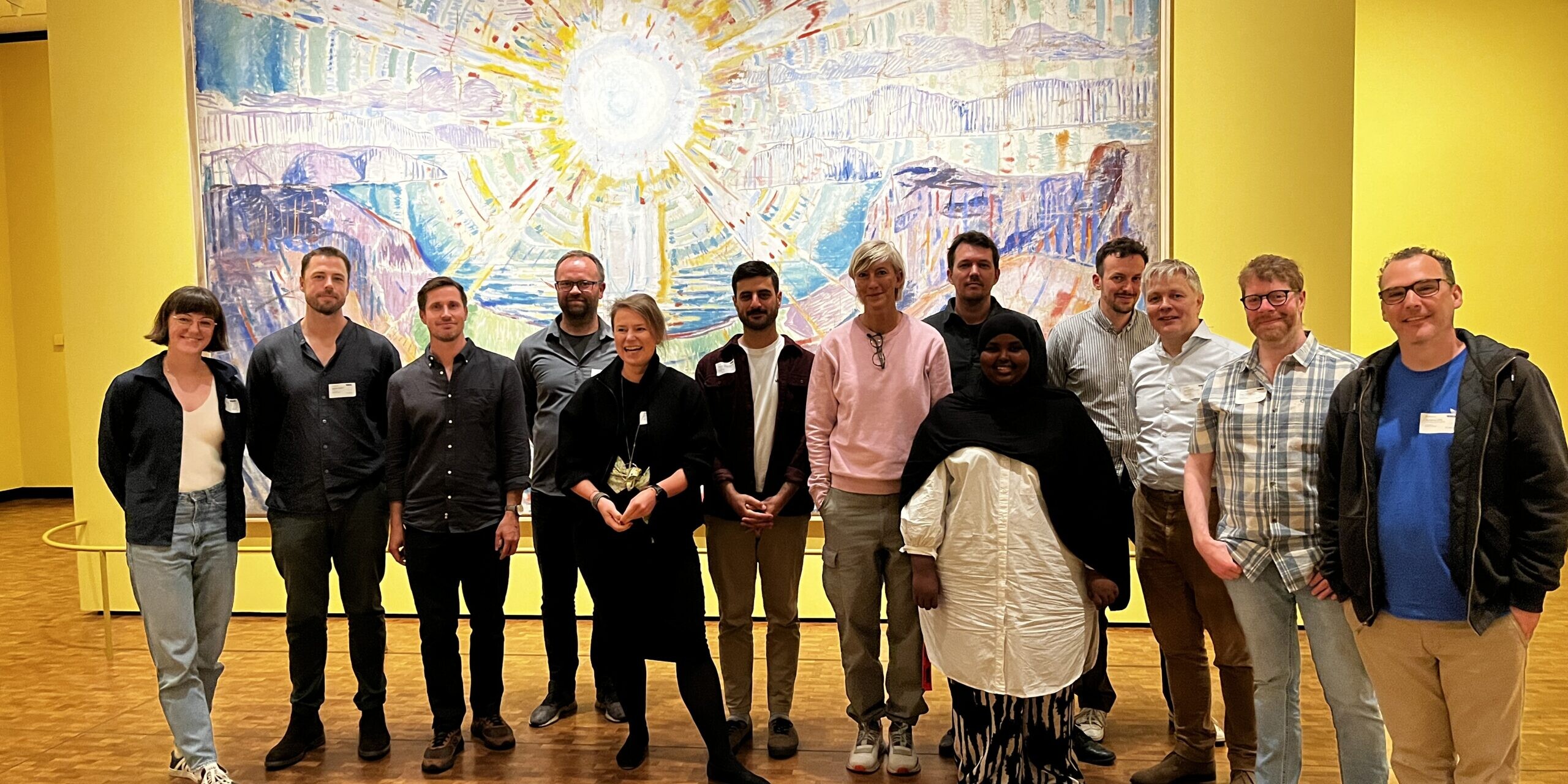 A group of people posing in front of a large painting. The painting depicts a sun.