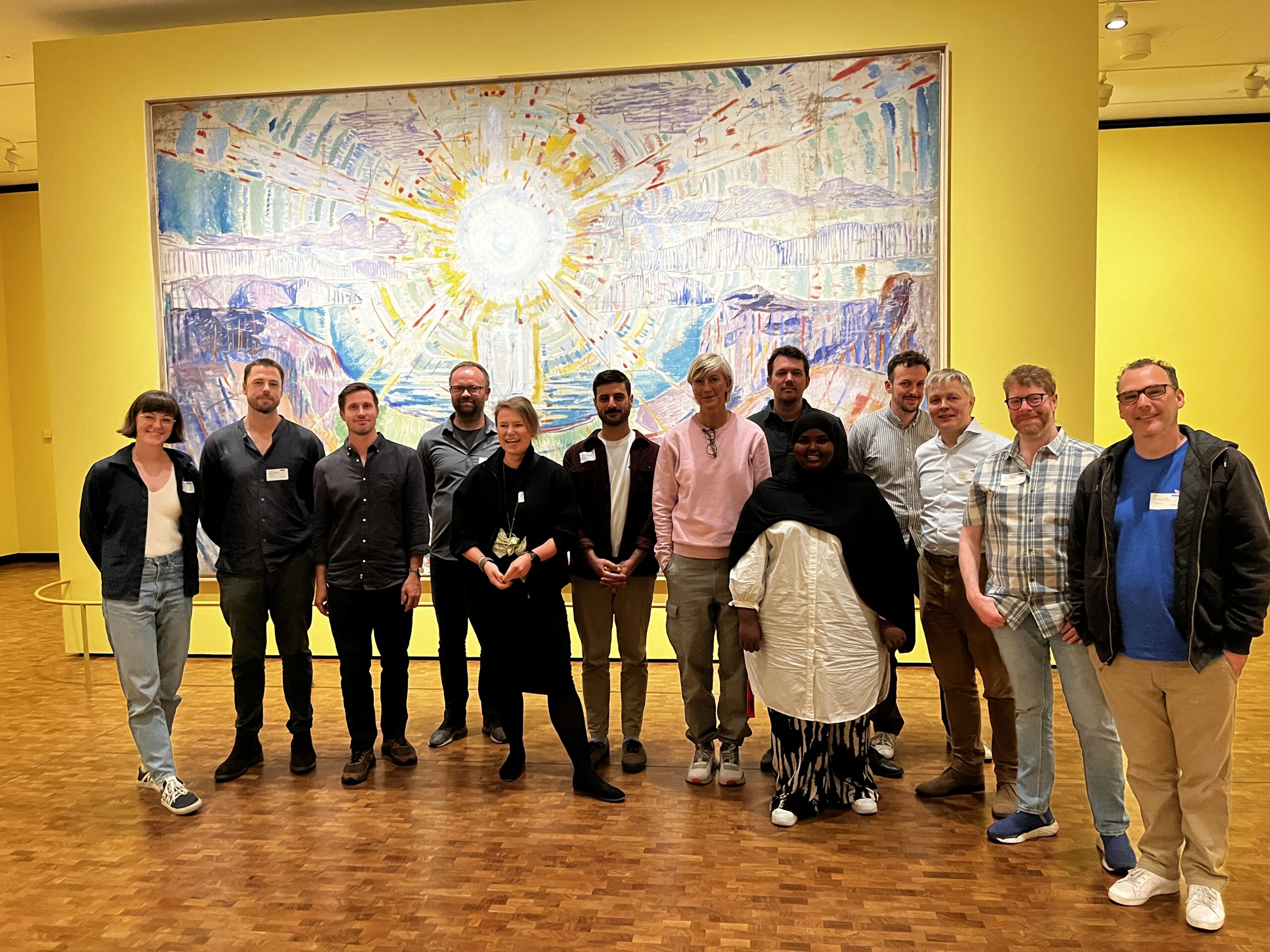 A group of people posing in front of a large painting. The painting depicts a sun.